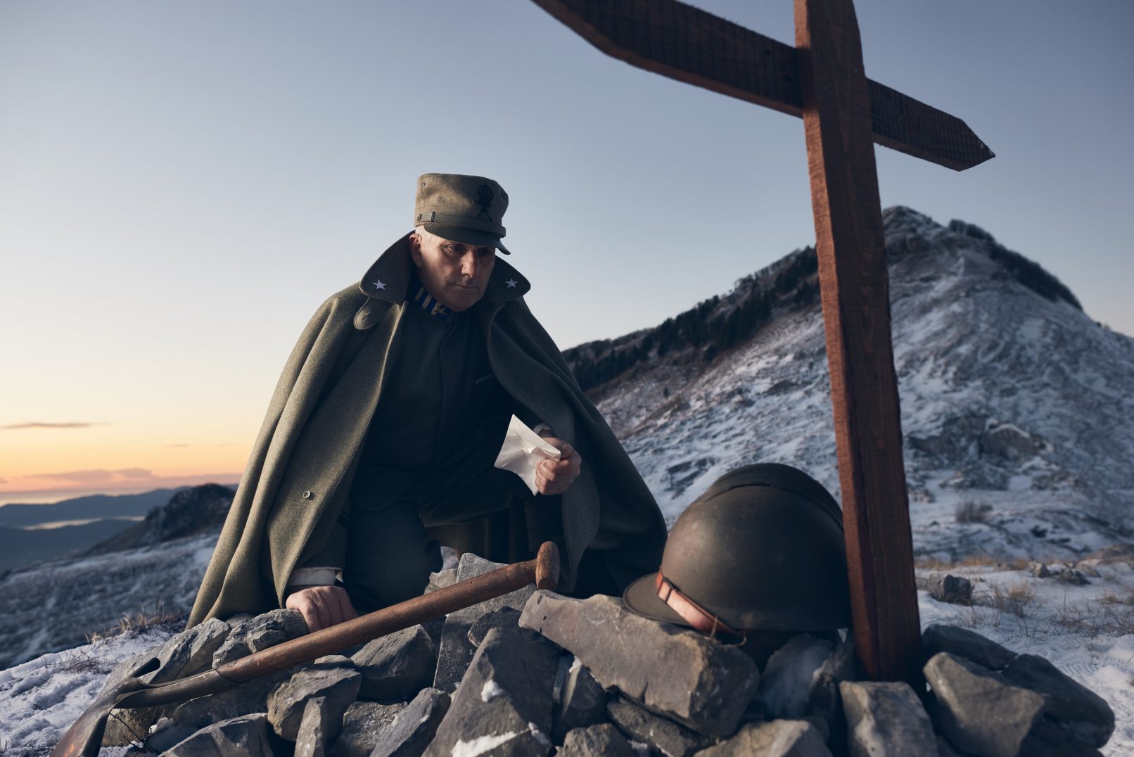 Portrait of Alberto Simonelli wearing a World War I Italian Infantry Man Uniform. Image shot on Monte Sagro, Tuscany, Italy showing Alberto looking a a cross and army helmet surrounded by swan during sunset.Personal project dedicated to historic portraits. Image series by David Umberto Zappa - portrait, commercial and advertising photographer. Ritratto di Alberto Simonelli, in uniforme militare Mitragliere Italiano Prima Guerra Mondiale. Immagine scattata sul Monte Sagro, Toscana. Alberto chino su una croce ed elmetto circondato da neve sotto le luci del tramonto. Progetto personale del fotografo commerciale, pubblicitario, ritrattista ed editoriale David Umberto Zappa.