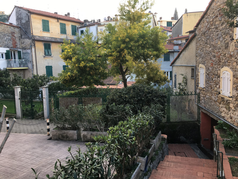 scalinata con vista su corte interna tra palazzi dai tipici colori liguri, verso Via Roma in centro a Lerici, Liguria. Case e volti in pietra con alberi in fiore.