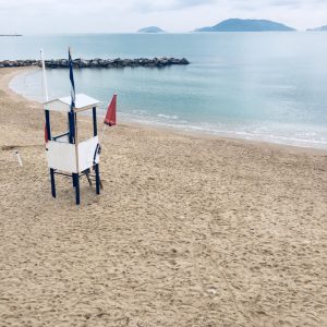 Lerici, spiaggia Venere Azzurra. Torretta bagnino bianca con bandiera Mare Blu ed ombrellone rosso. All'orizzonte isole Tino, Palmaria e scorcio di Portovenere.