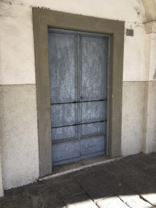 Via del Torrione Genovese Sarzana portone antico color celeste con barre di ferro orizzontali sotto un portico