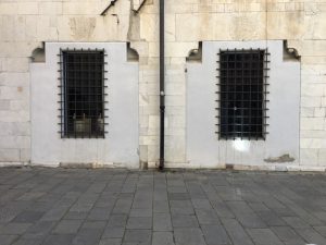 Piazza Matteotti Sarzana. Facciata con grandi finestre con inferiate. Cornice in marmo bianco e muro in pietra.