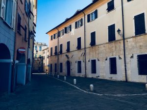Piazza Matteotti Sarzana con facciate di palazzi storici e portici sul lato sinistro. Inferiate e portoni. Location Scout duzimage