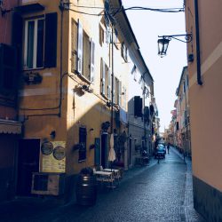 Via Mascardi a Sarzana con pavimentazione in sanpietrini, ristorante sulla sinistra con botte in legno e tavolini. Vista direzione sud. Location scout