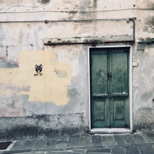 Sarzana, muro in stato decadente con portone in legno verde, accenni di pittura gialla e stencil. Parete nei pressi di Piazza Matteotti fotografata per location scouting italia - duzimage