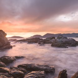 tramonto sul Golfo dei Poeti visto dagli scogli tra le due spiagge di Fiascherino. Scogli in primo piano ed acqua del mare tinta di viola. Cielo nuvoloso. Location scout italia - duzimage