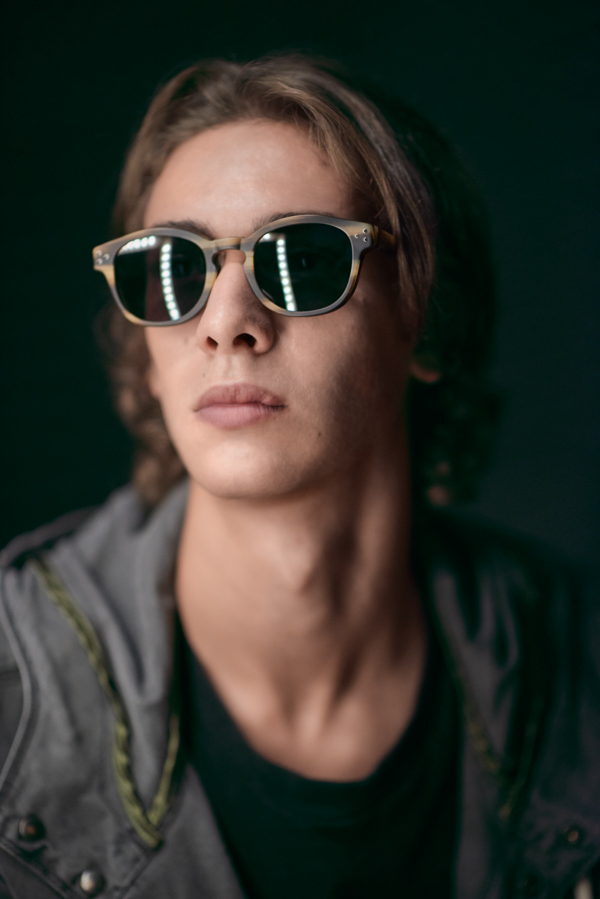 male model wearing sunglasses on a dark background with led lighting reflected on the lenses