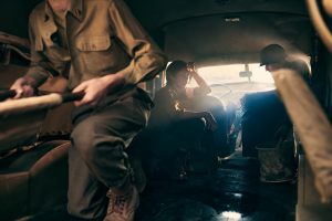 interior of a WWII ambulance with three soldiers, one of them is a woman touching her forehead lit by late afternoon warm light.