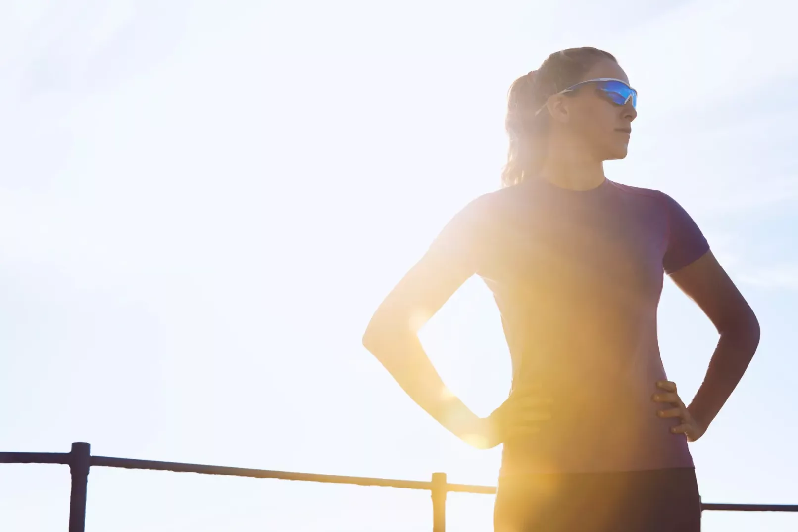 Portfolio Sport & Lifestyle del fotografo duzimage - ragazza in tenuta da running in piedi con le braccia sui fianchi, occhiali da sole e luce suggestiva alle sue spalle